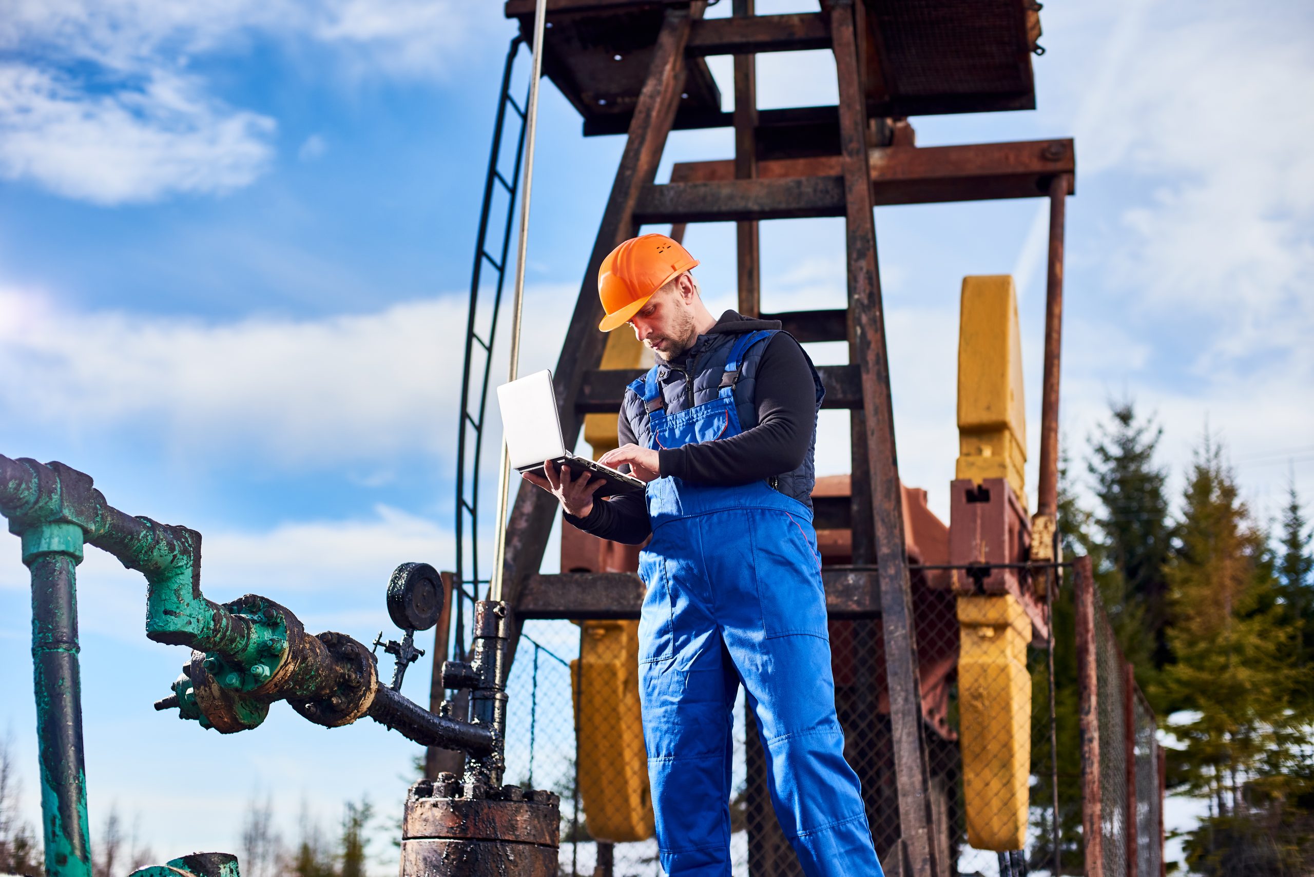 Petroleum engineer using laptop in oil field.